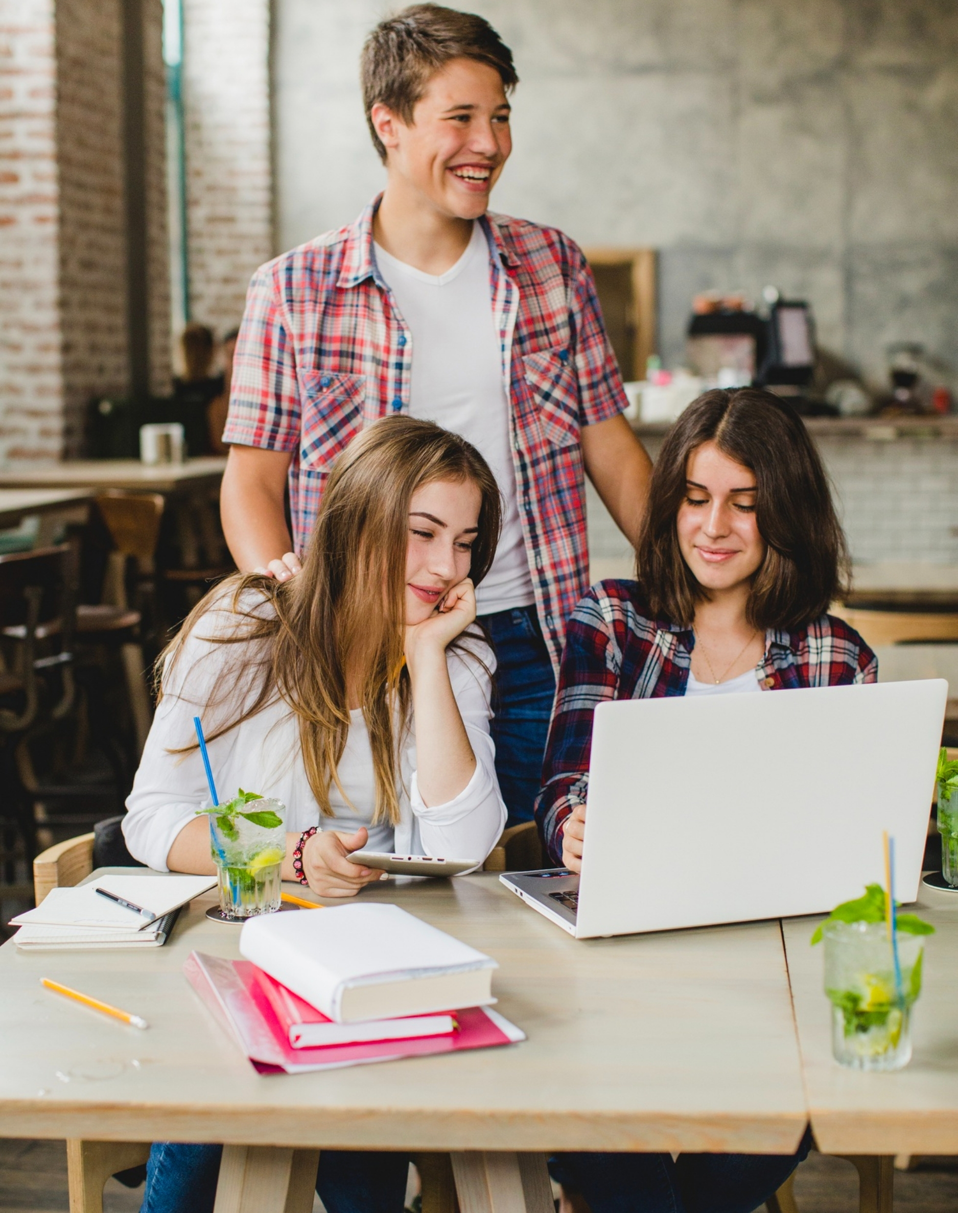 Joyful group of young Pakistani students collaborating on a laptop in a cozy cafe setting, representing interactive group sessions at GS Trainings for Forex, Crypto, and digital earning courses.